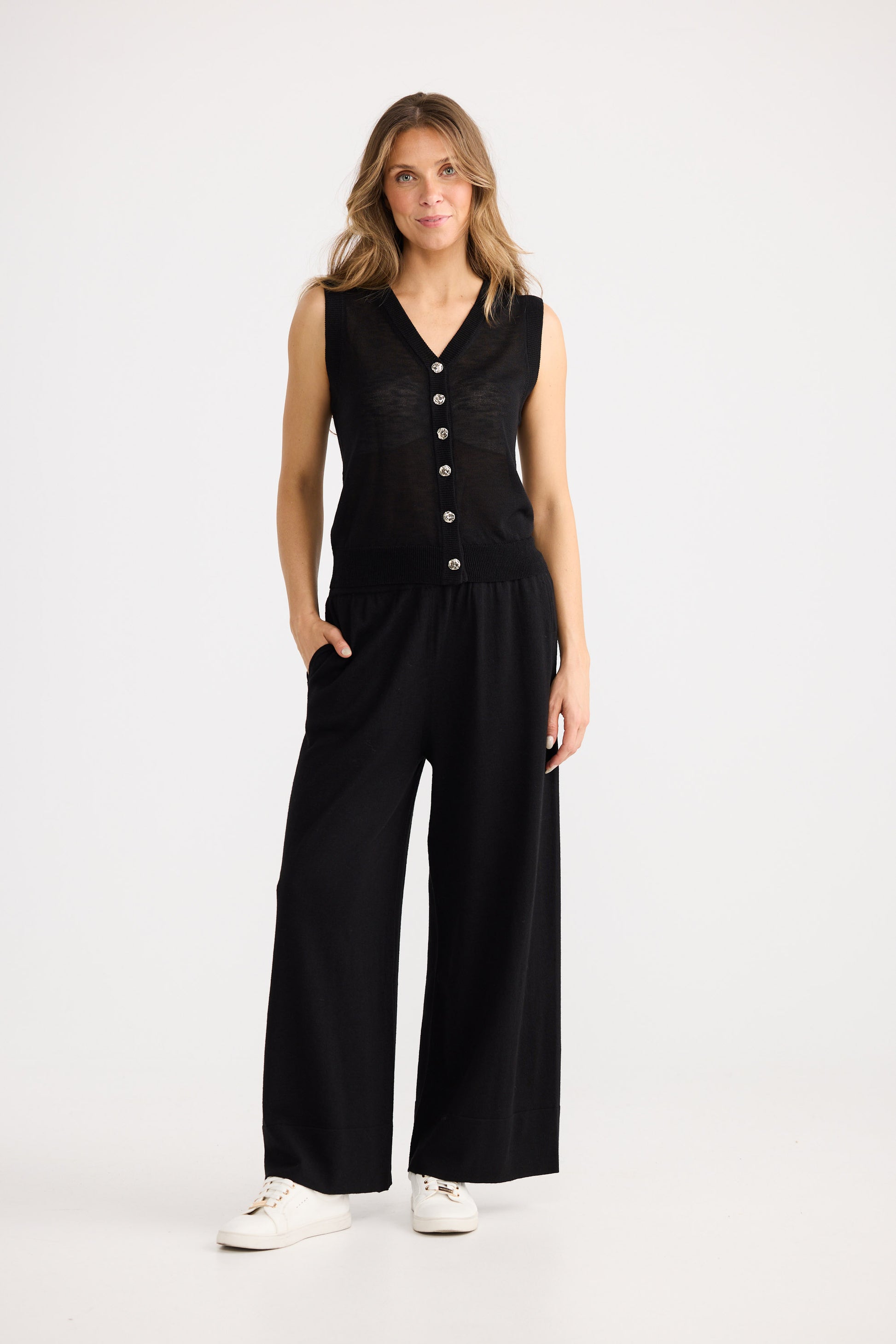 Woman wearing a black sleeveless jumpsuit with buttons on a white background