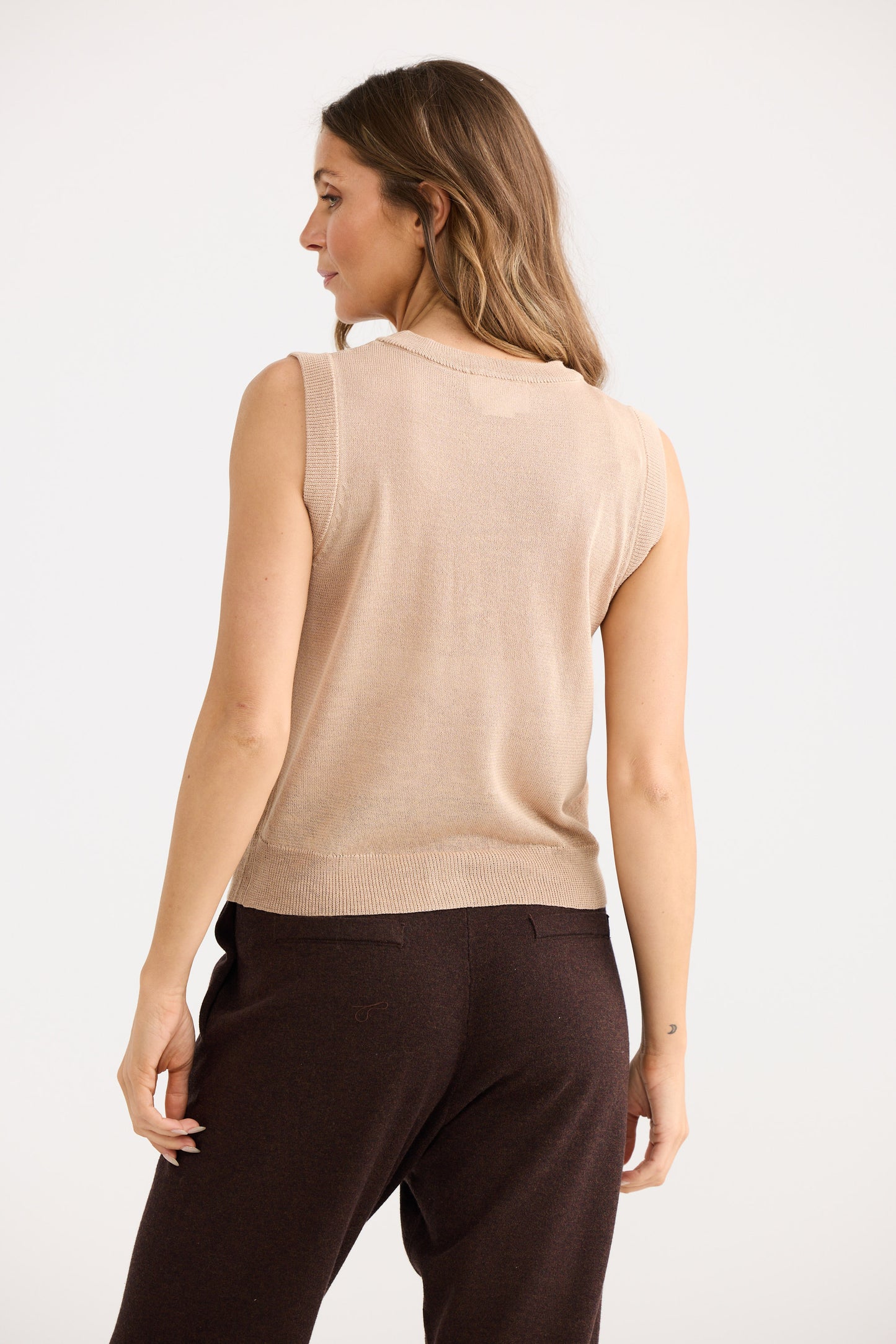 Woman wearing a beige sleeveless top and brown pants on a white background