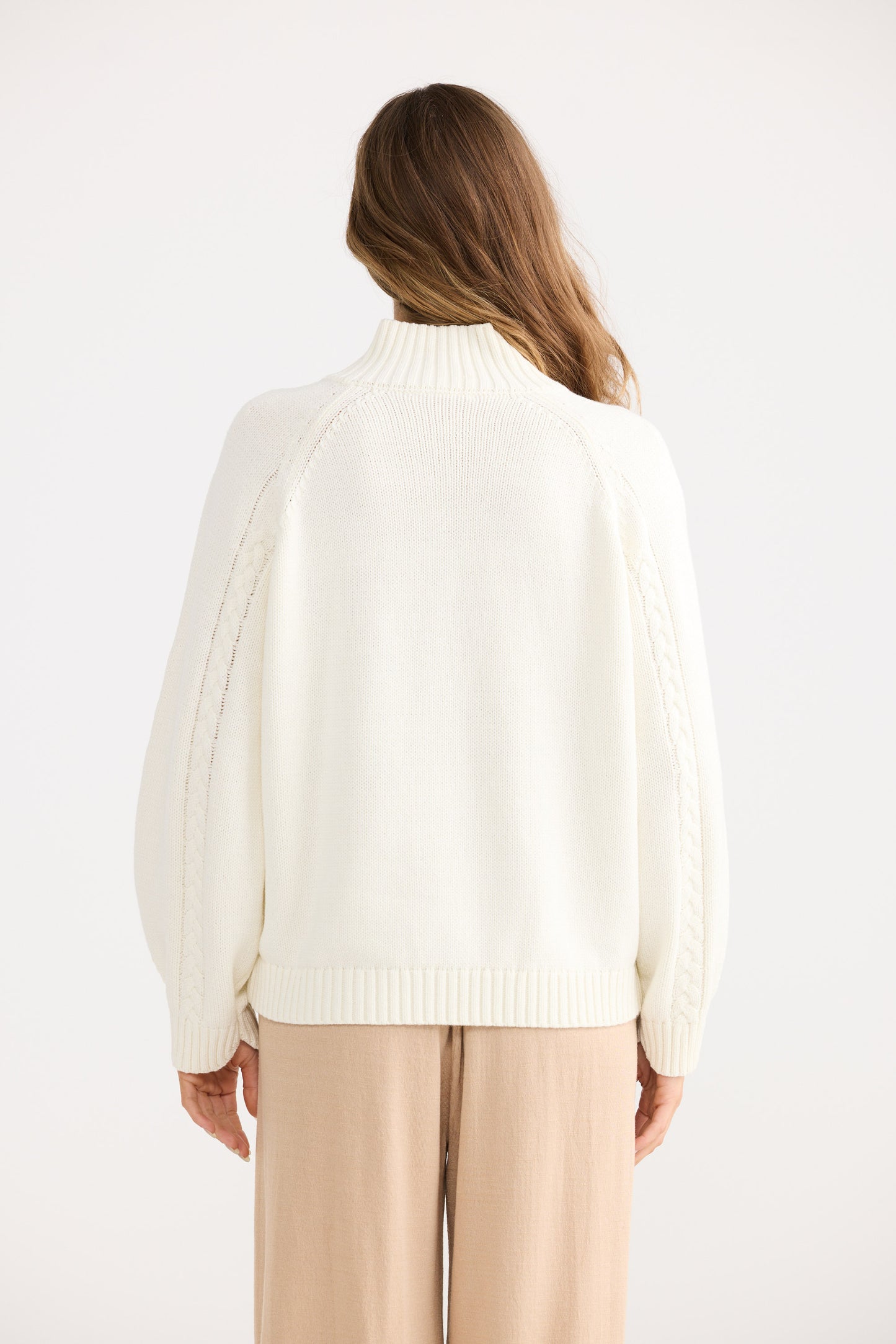 Person wearing a white sweater on a plain background