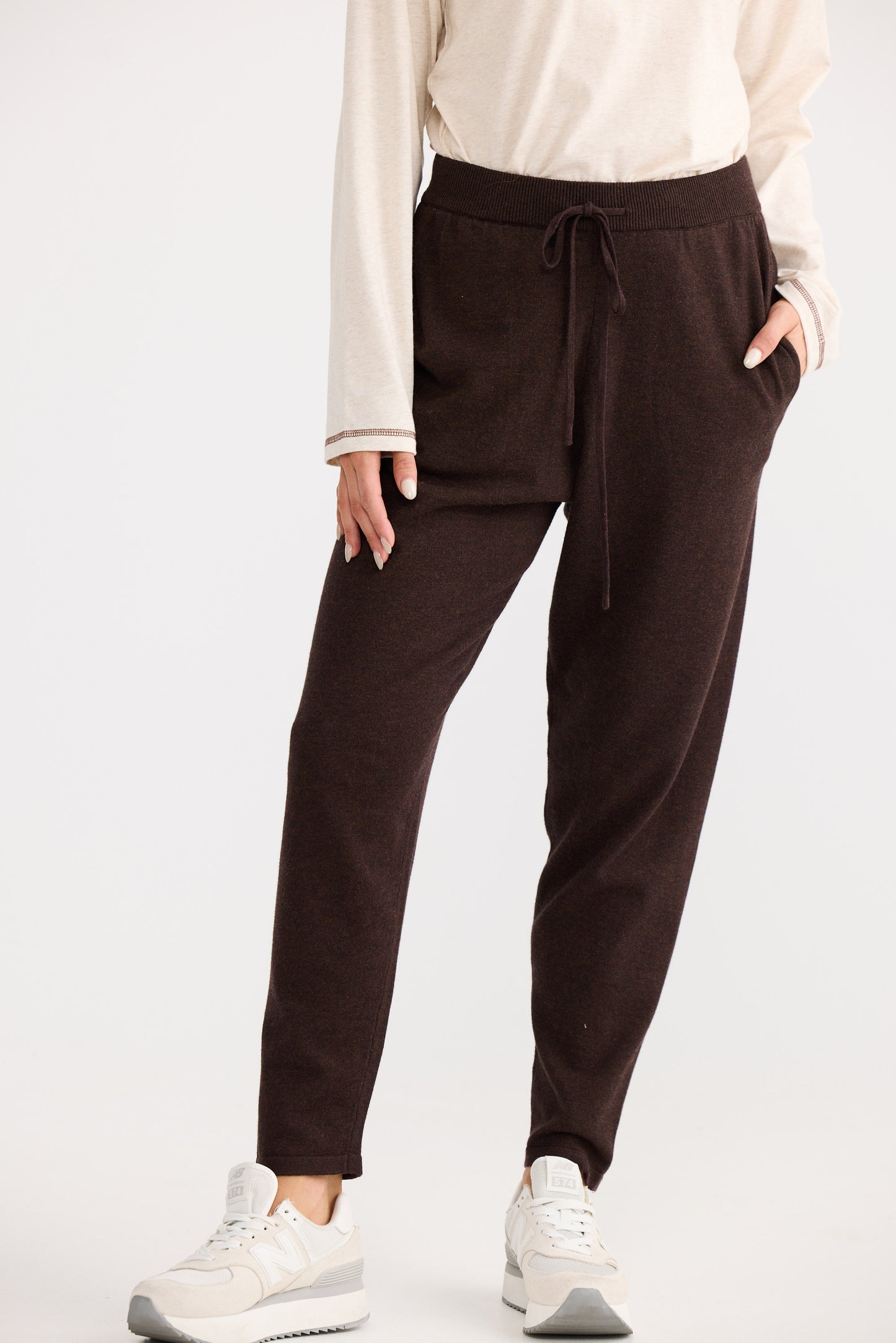 Person wearing brown sweatpants and a cream top on a white background