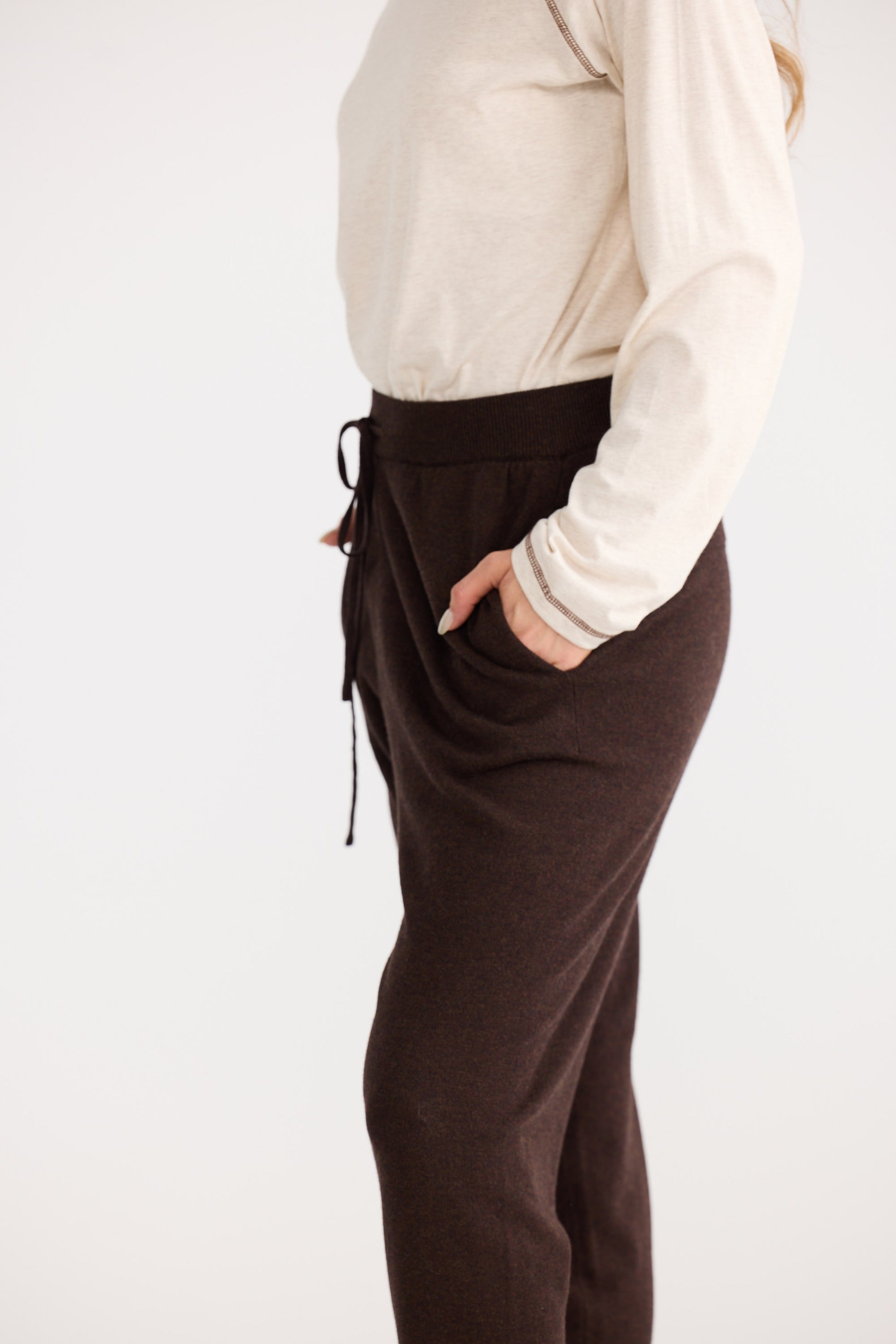 Person wearing brown pants and a white long-sleeve shirt on a white background