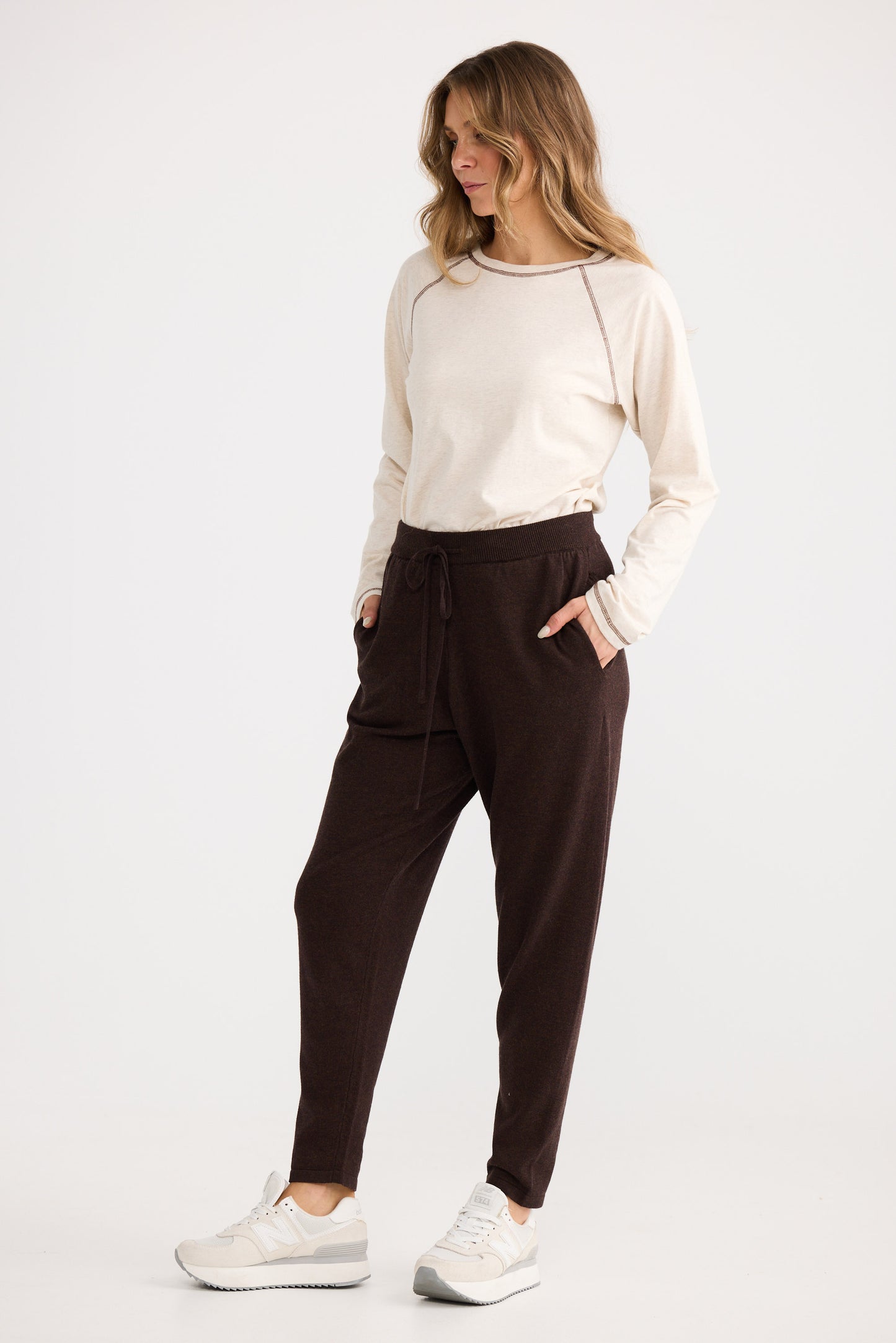 Woman wearing a white long-sleeve top and brown pants on a white background
