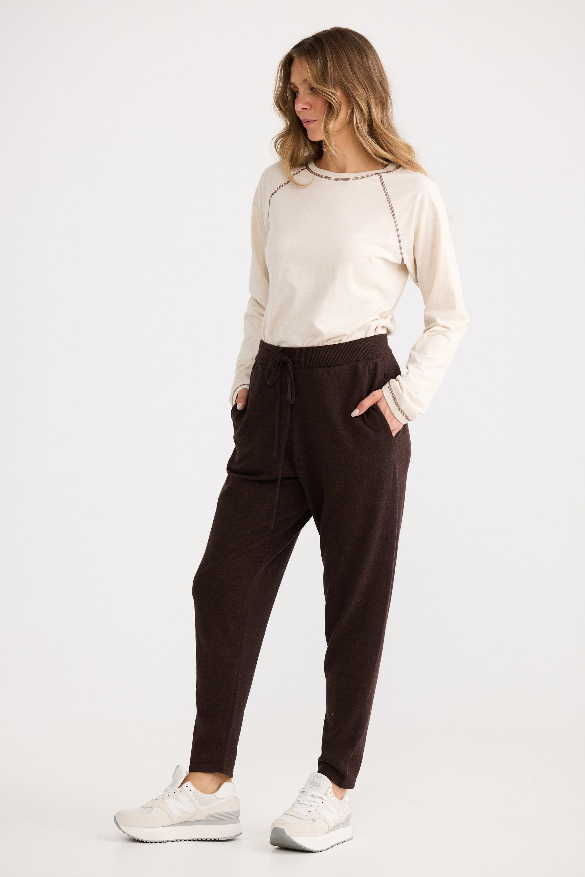 Woman wearing a white long-sleeve top and brown pants on a white background