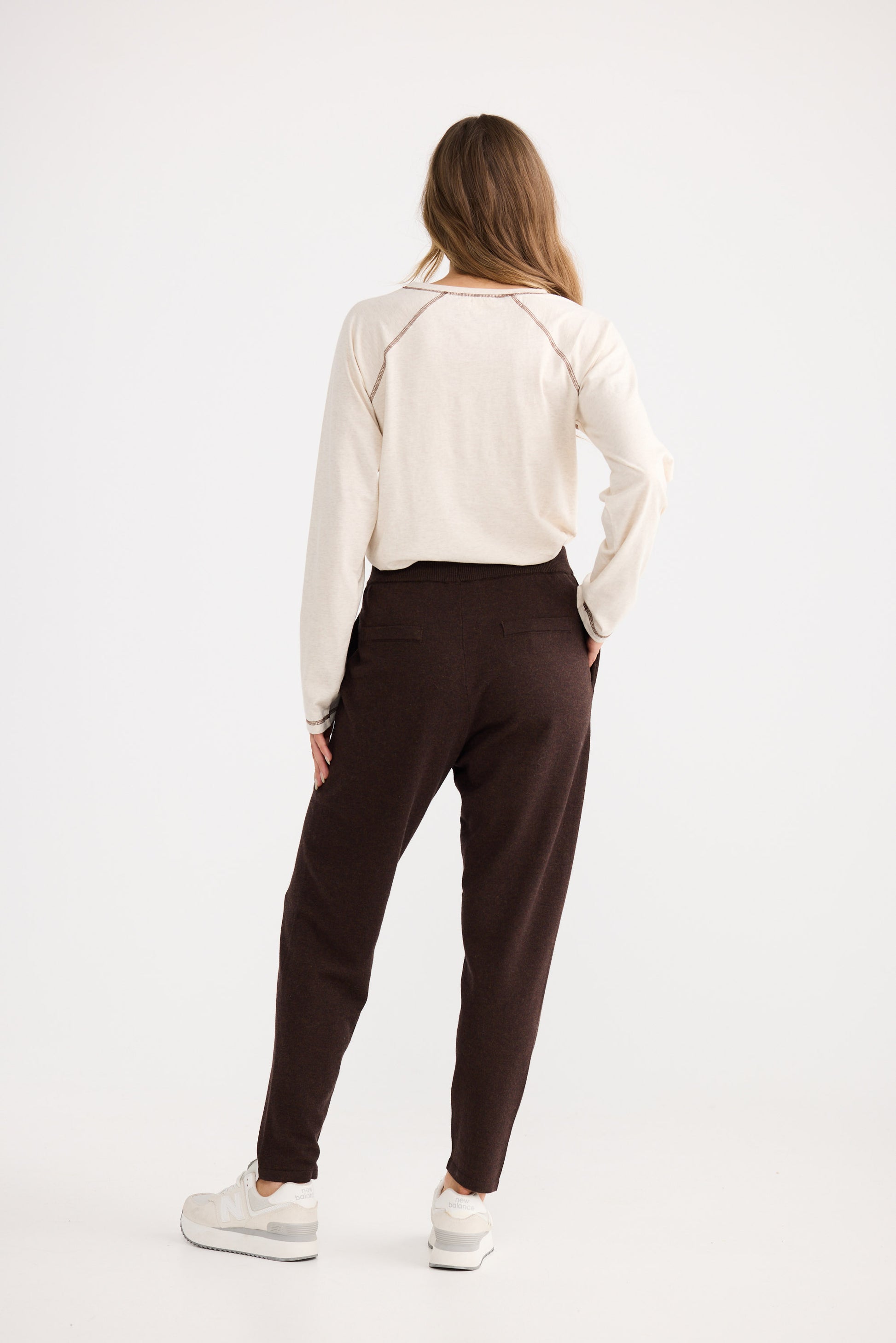 Person wearing a white sweater and brown pants on a white background