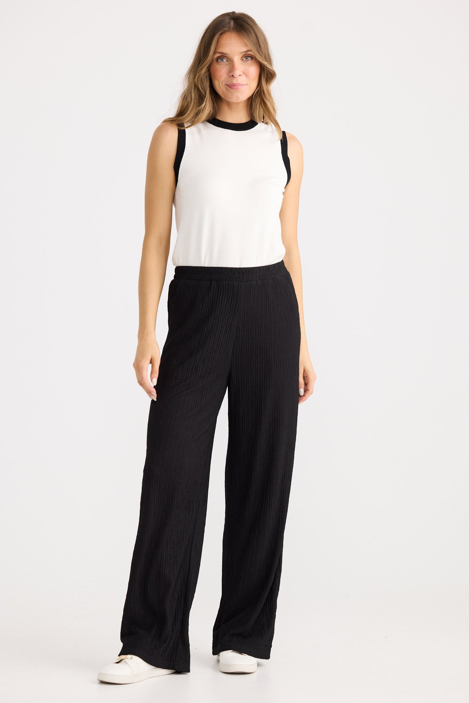 Woman wearing a white sleeveless top and black wide-leg pants on a white background