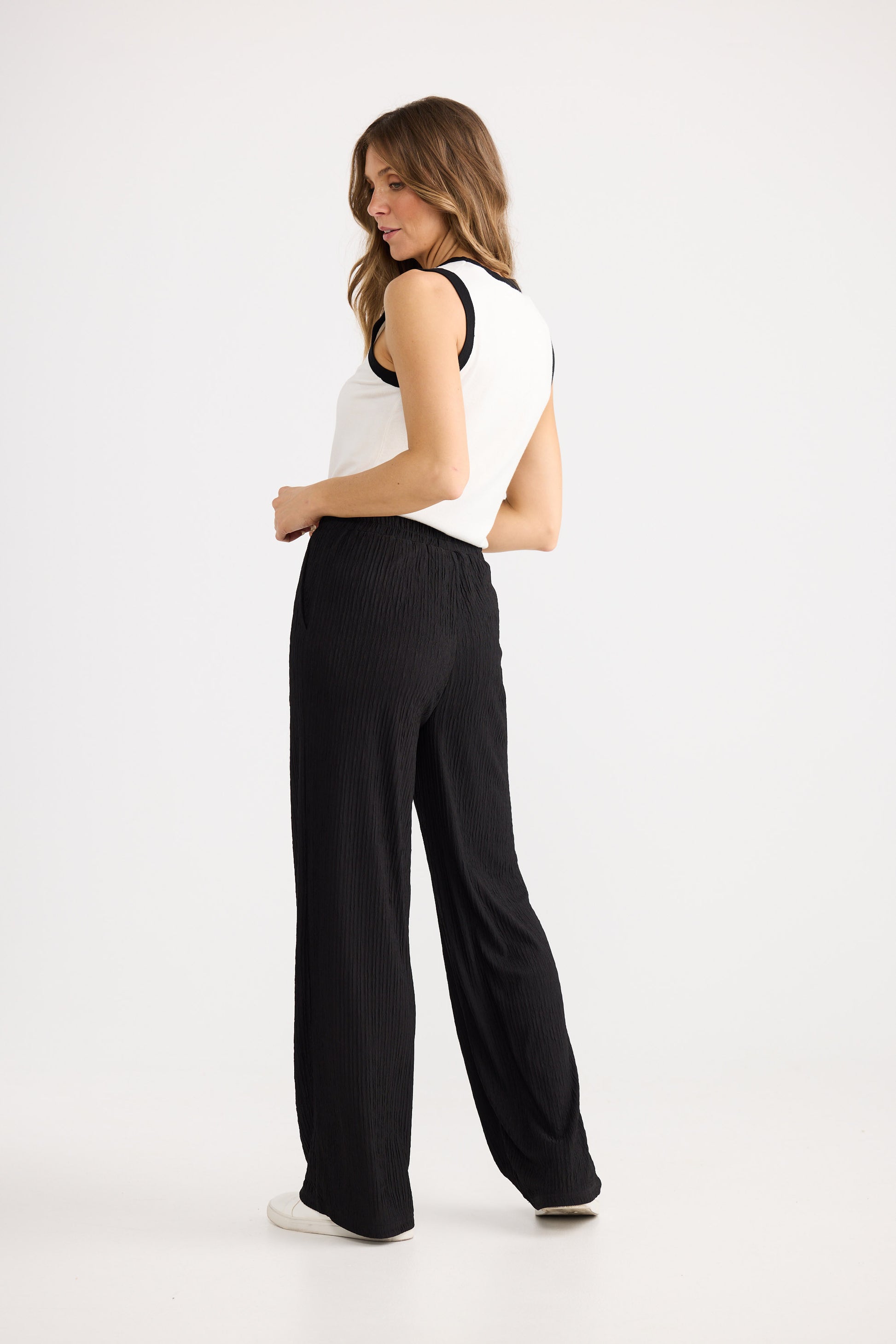 Woman wearing a white sleeveless top and black wide-leg pants on a white background