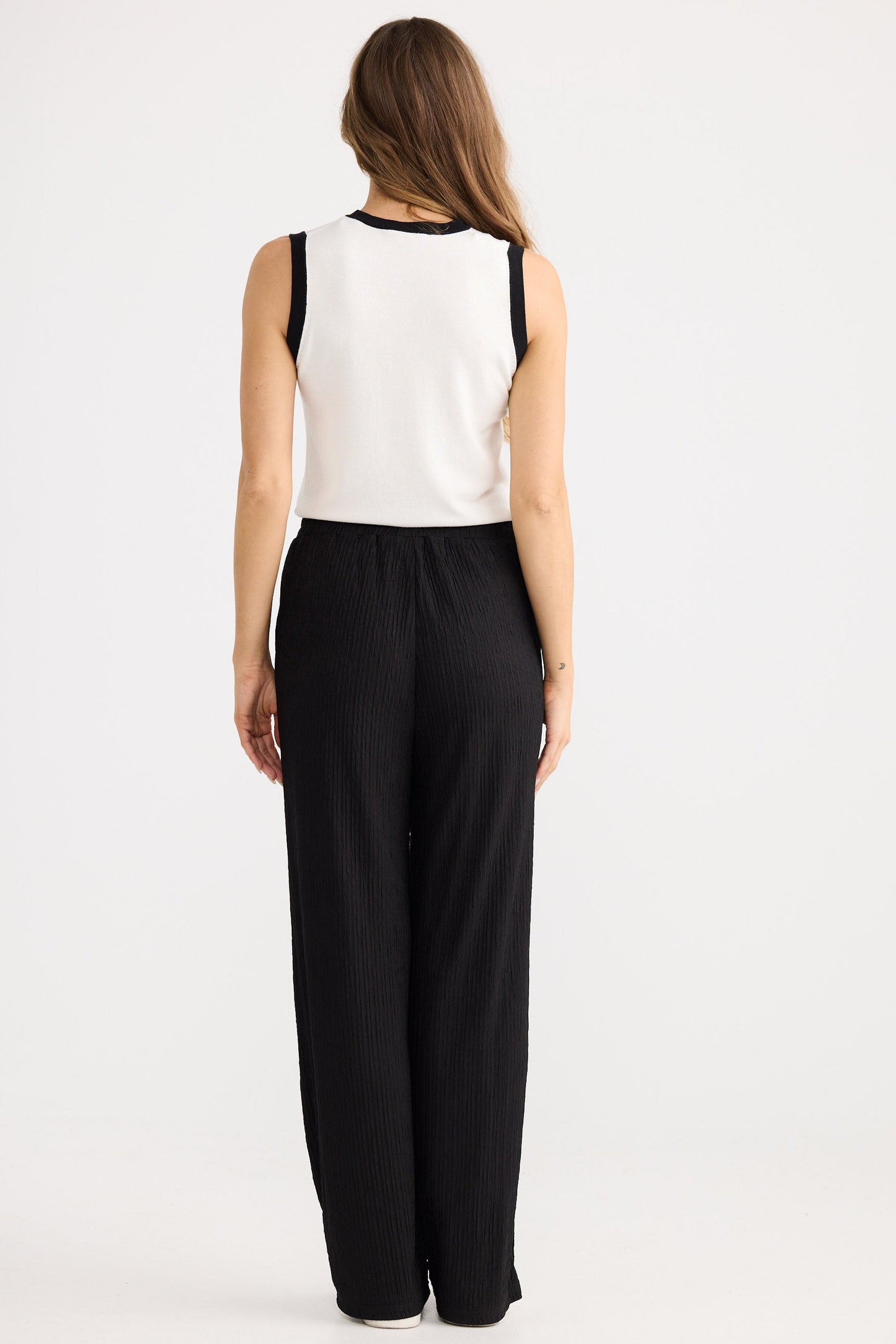 Woman wearing a white sleeveless top and black wide-leg pants on a white background