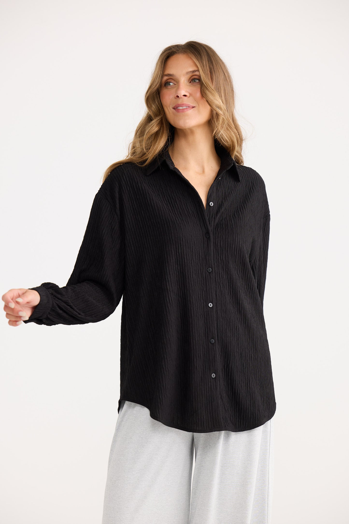 Woman wearing a black button-up shirt and white pants on a white background