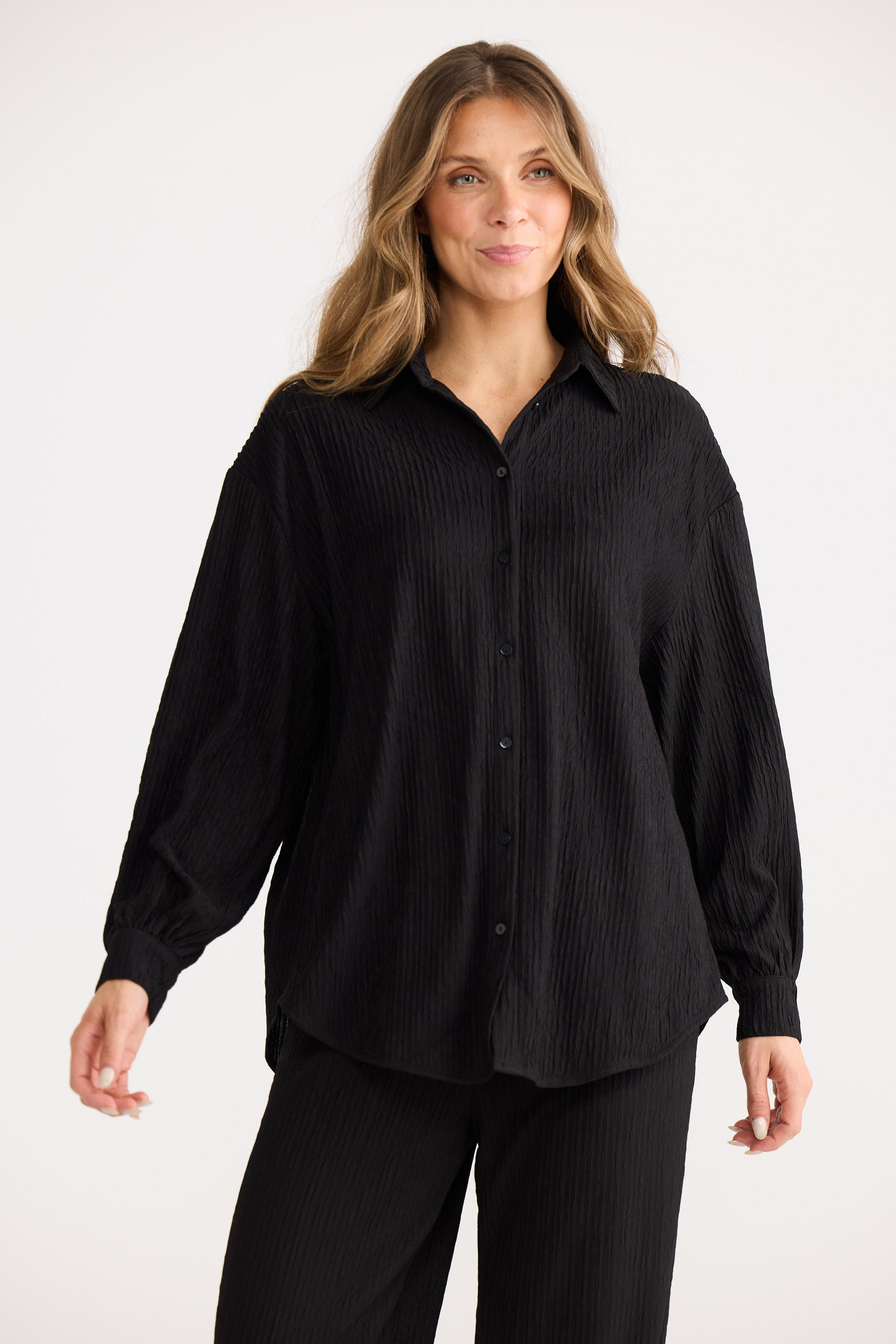 Woman wearing a black button-up shirt and black pants on a white background
