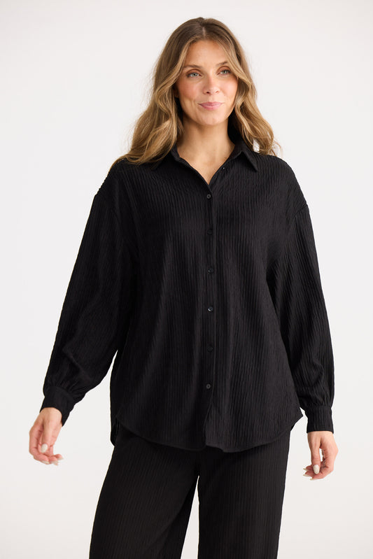 Woman wearing a black button-up shirt and black pants on a white background