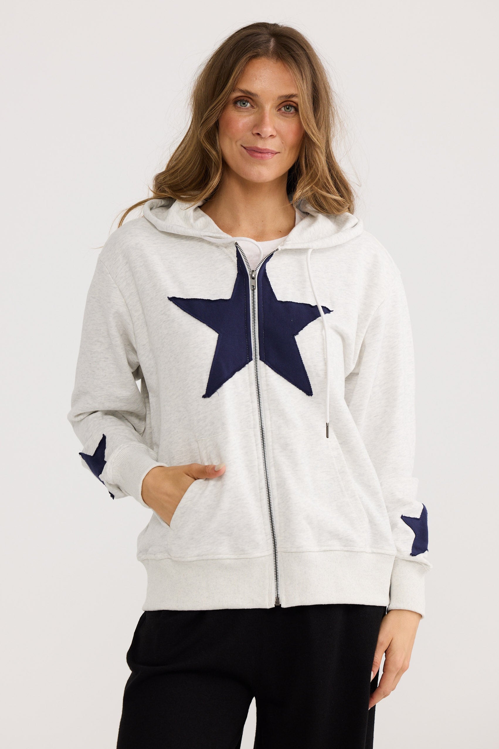 Woman wearing a white hoodie with a navy star design on a plain background