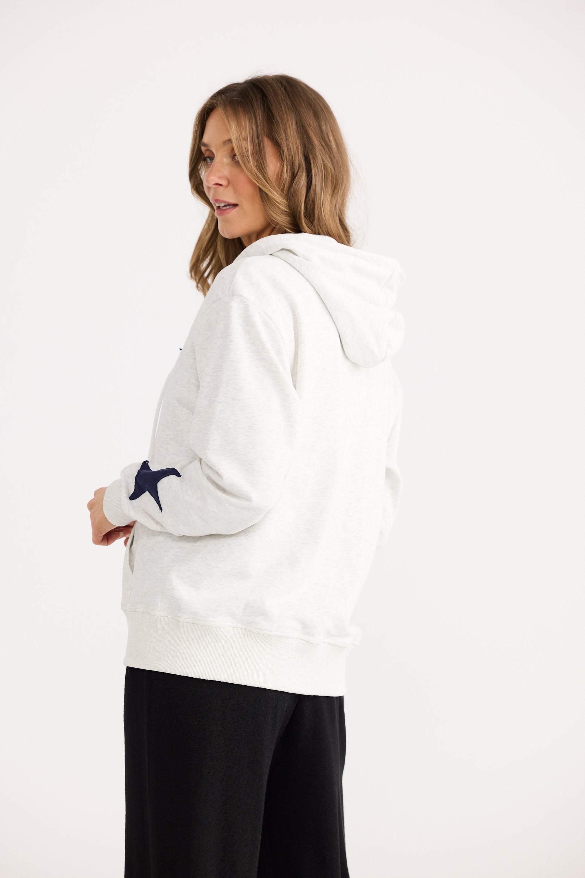 Woman wearing a white hoodie with a blue star design on a plain background