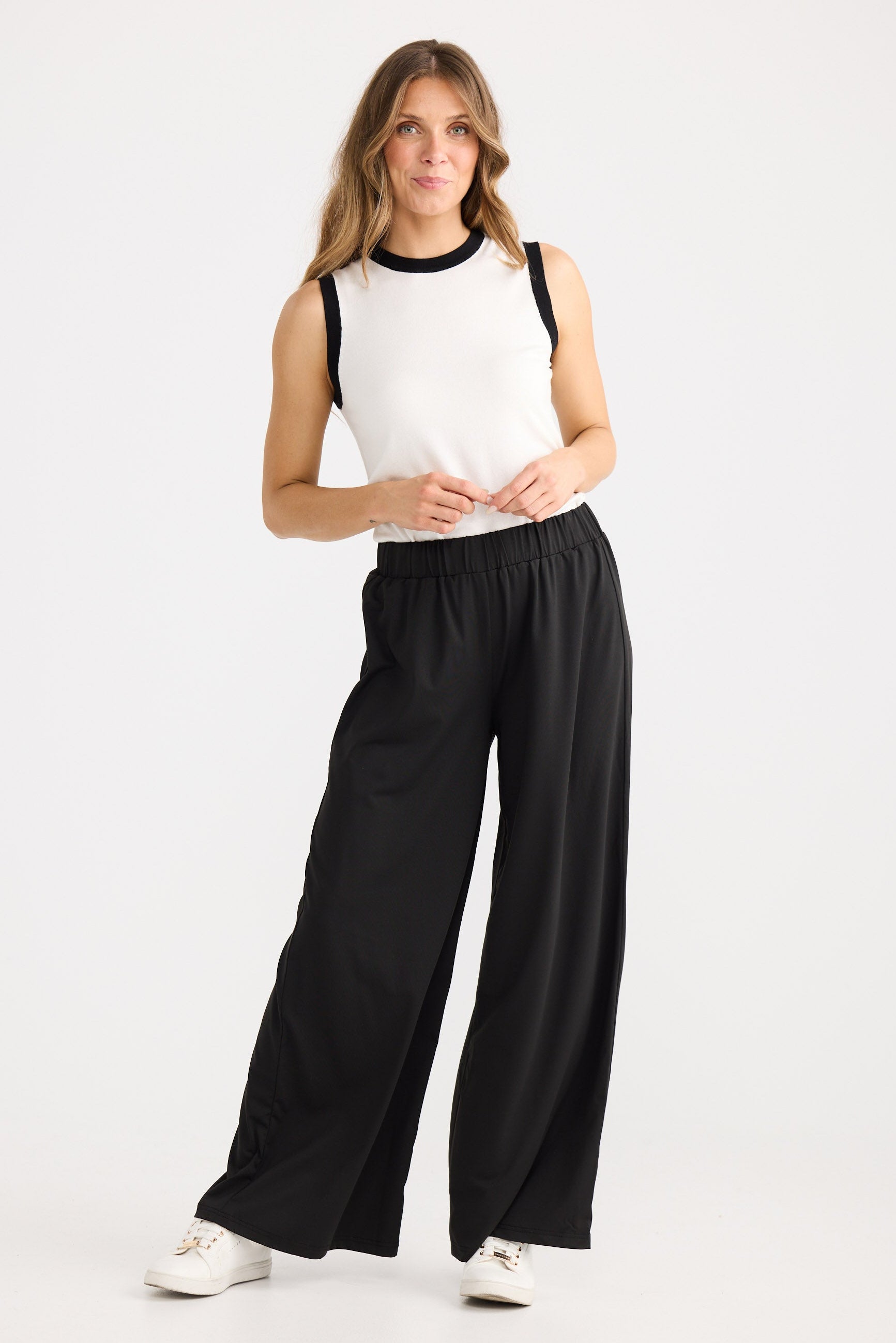 Woman wearing a white sleeveless top with black trim and black wide-leg pants on a white background