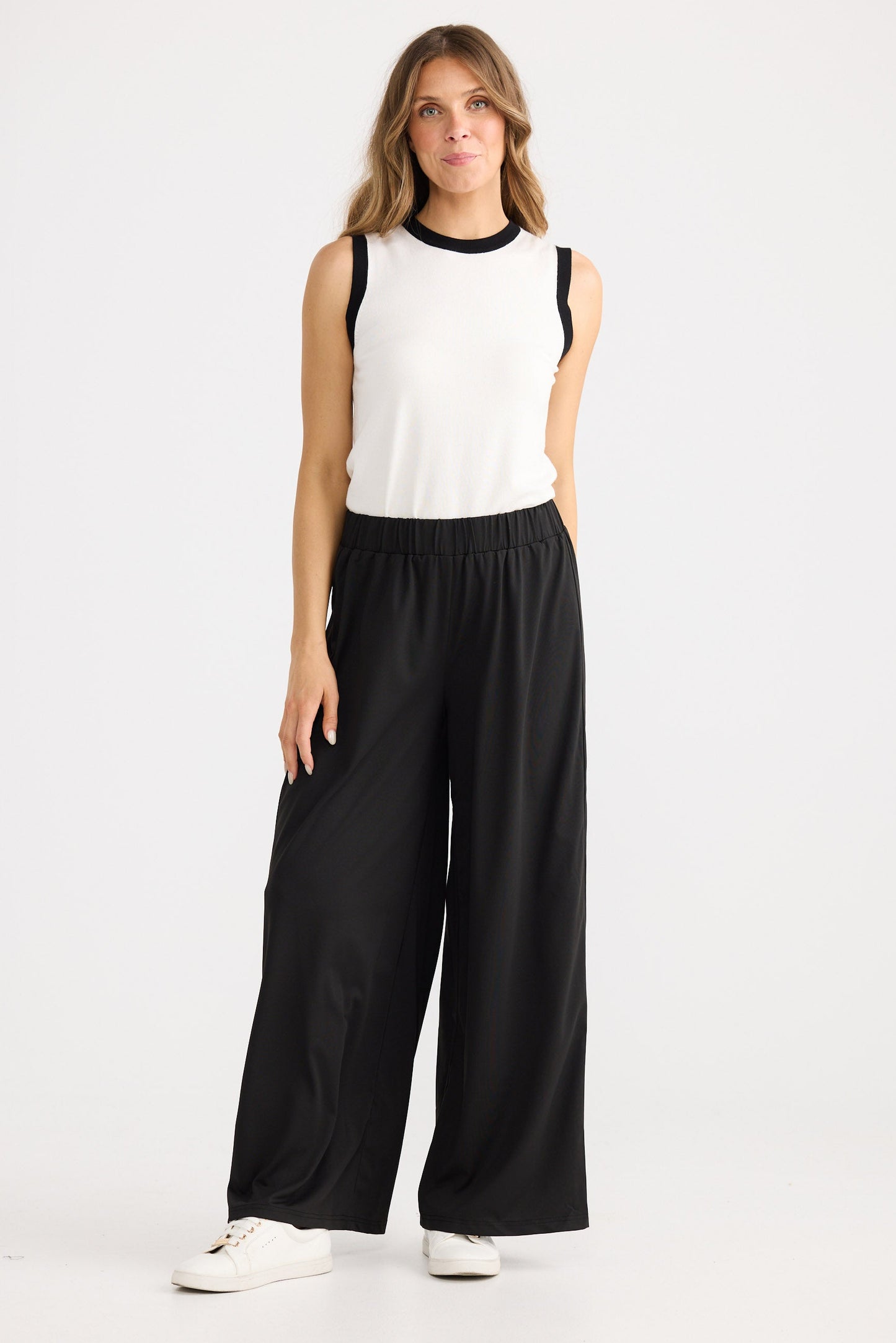 Woman wearing a white sleeveless top and black wide-leg pants on a white background