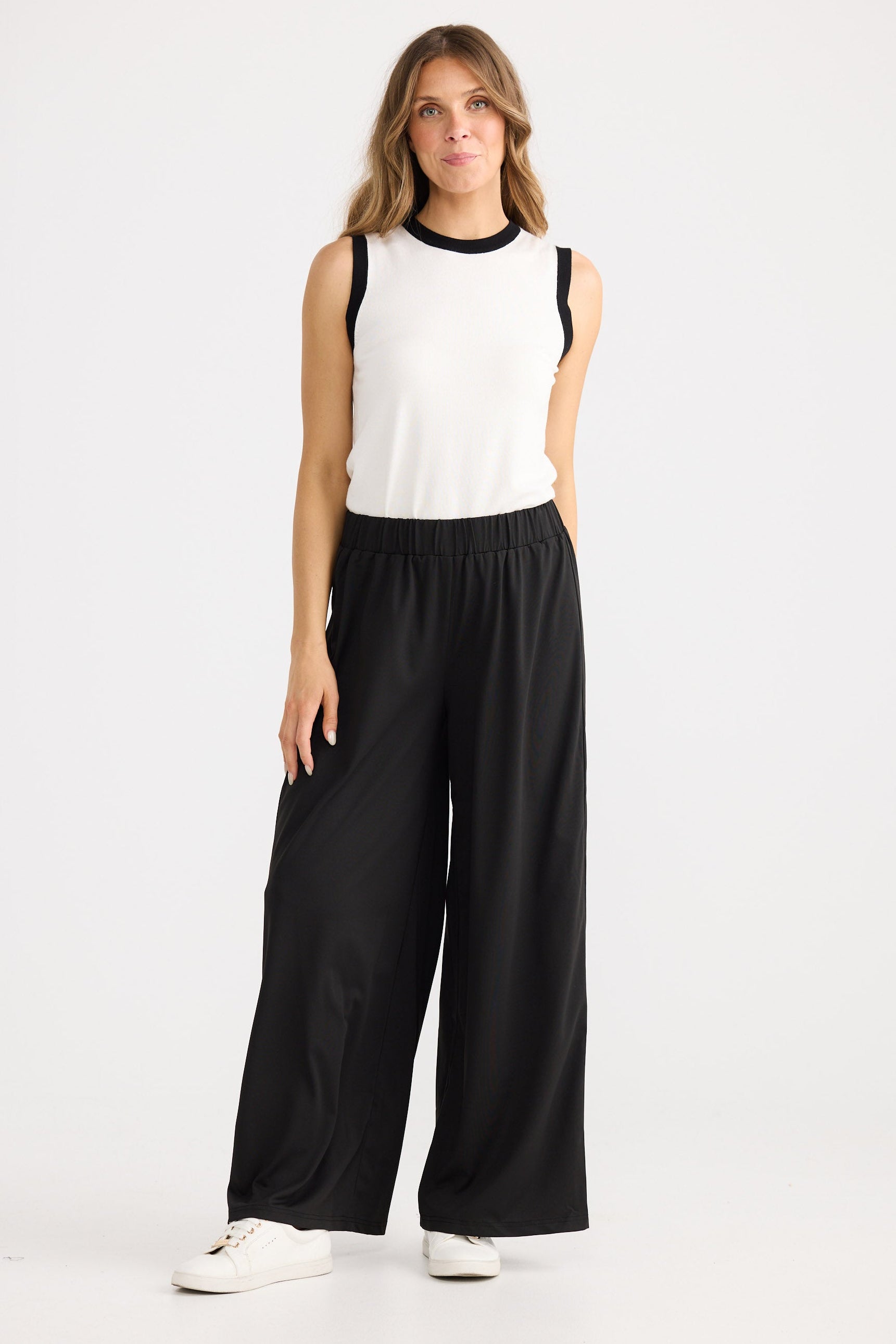 Woman wearing a white sleeveless top and black wide-leg pants on a white background