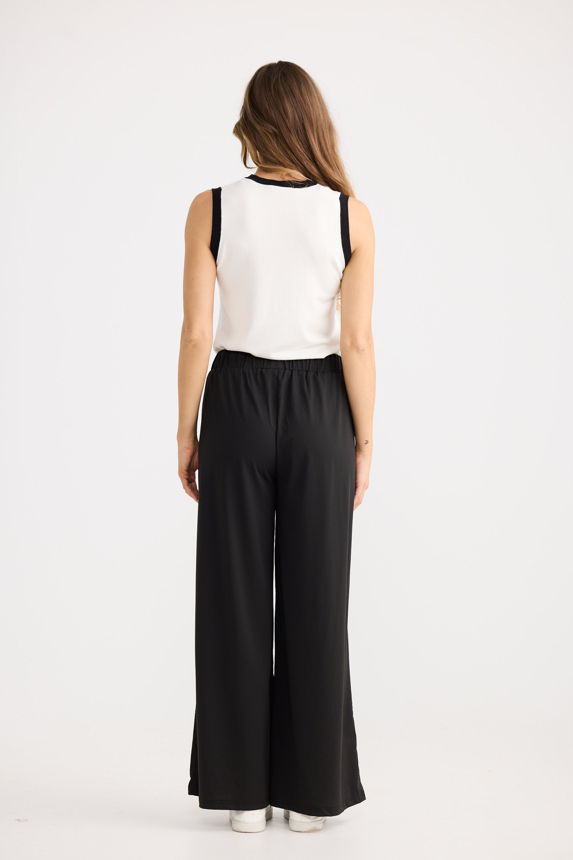 Woman wearing a white sleeveless top and black wide-leg pants on a white background