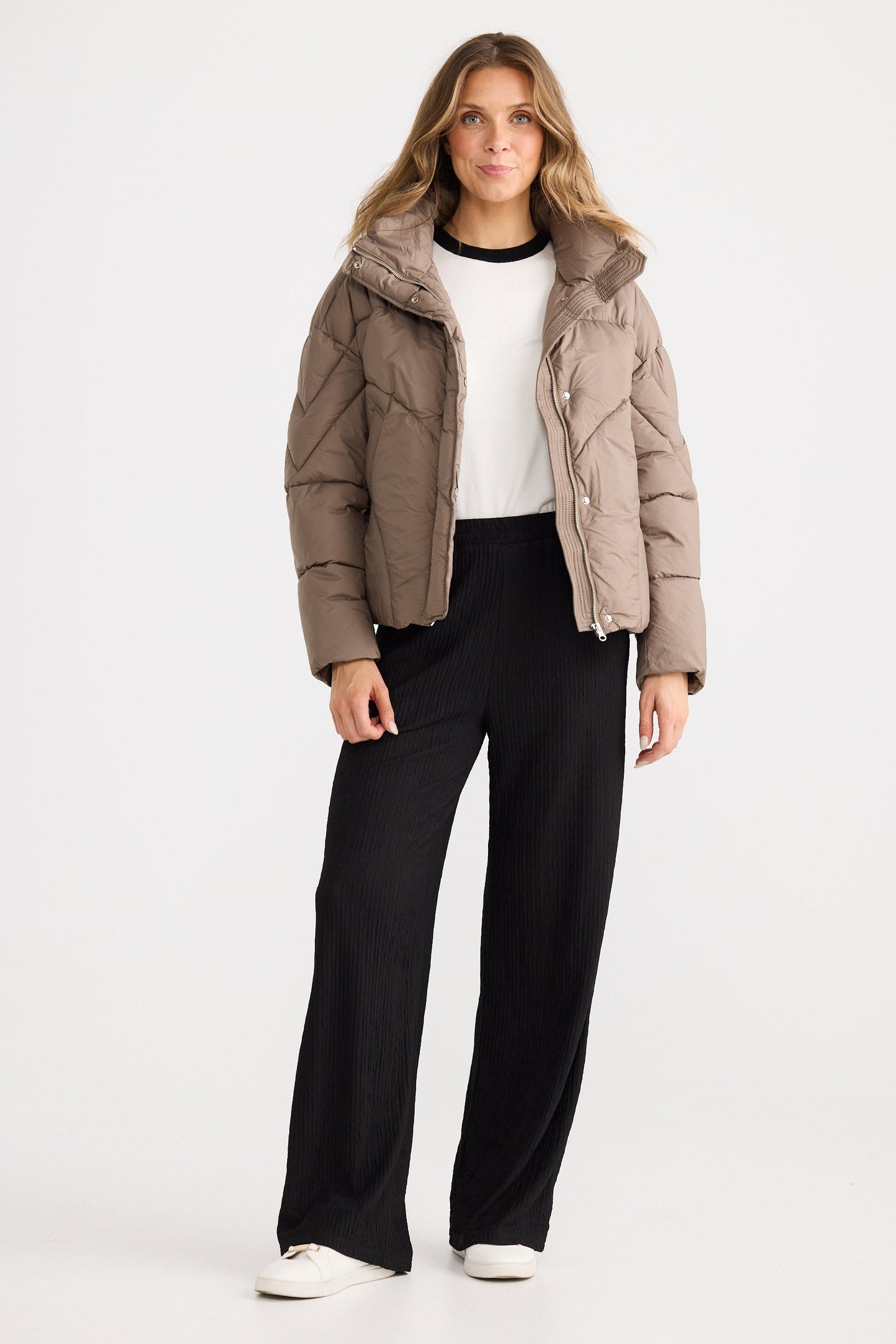 Woman wearing a beige puffer jacket and black pants on a white background