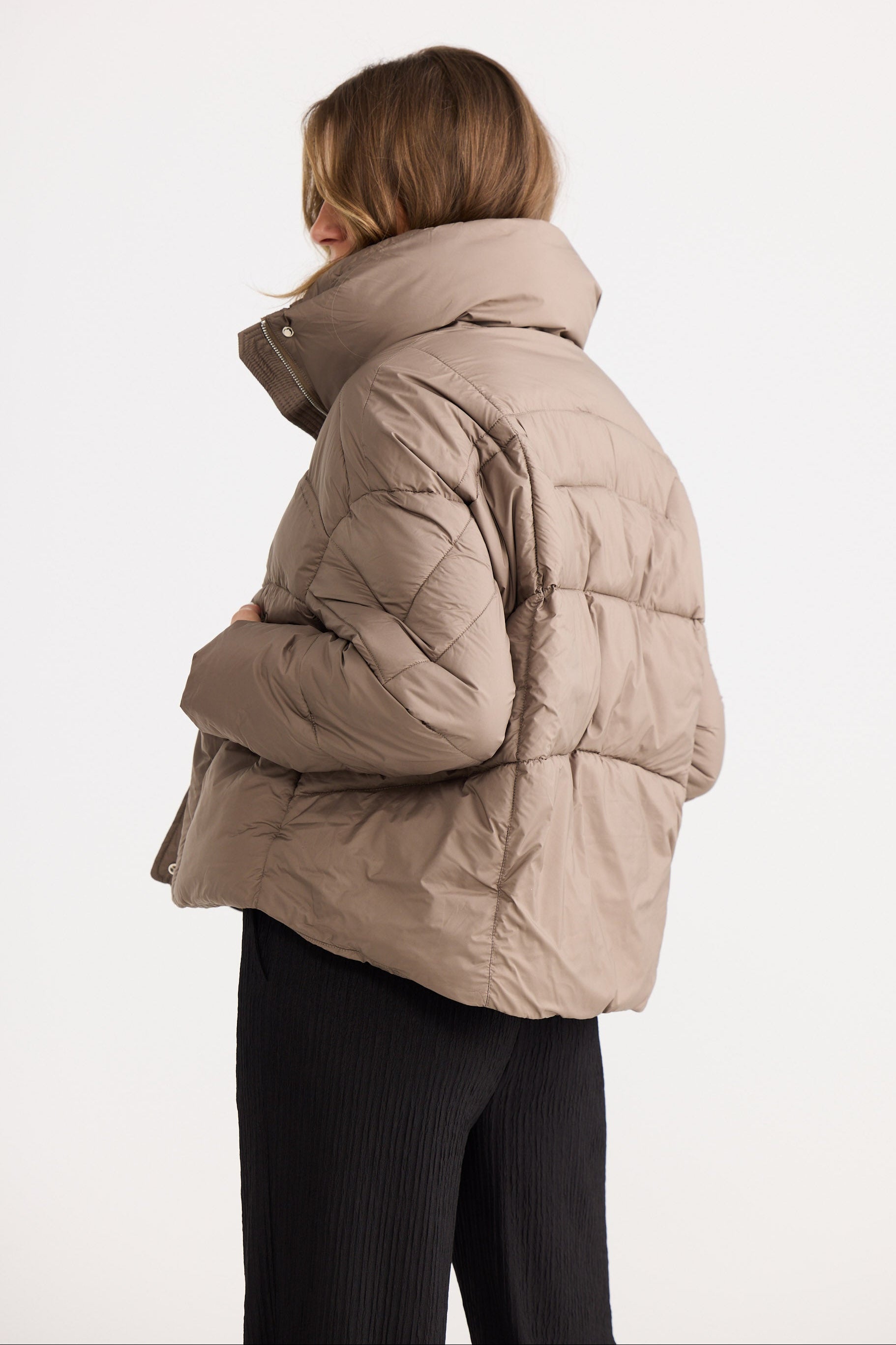 Person wearing a beige puffer jacket on a white background