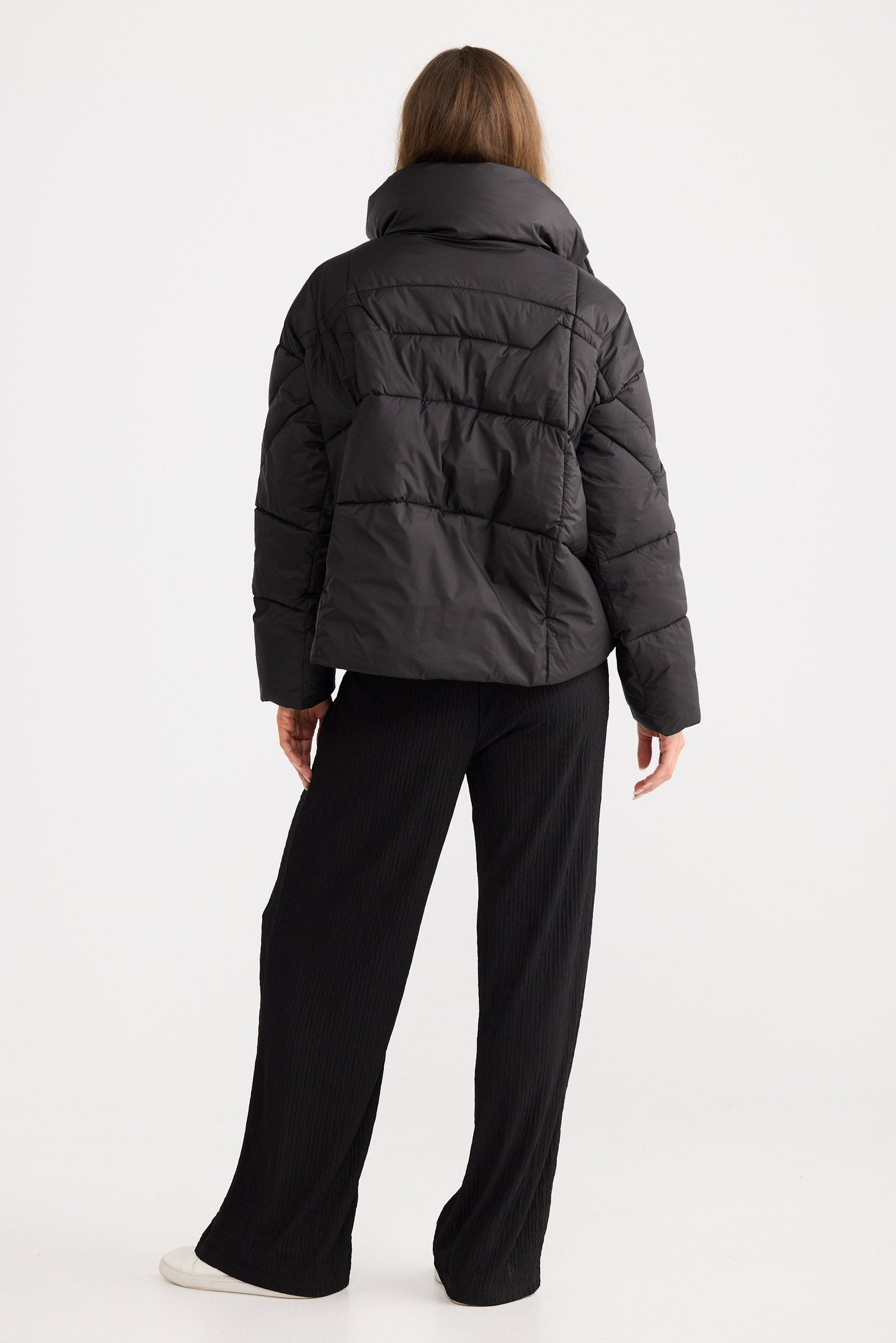 Person wearing a black puffer jacket and black pants on a white background