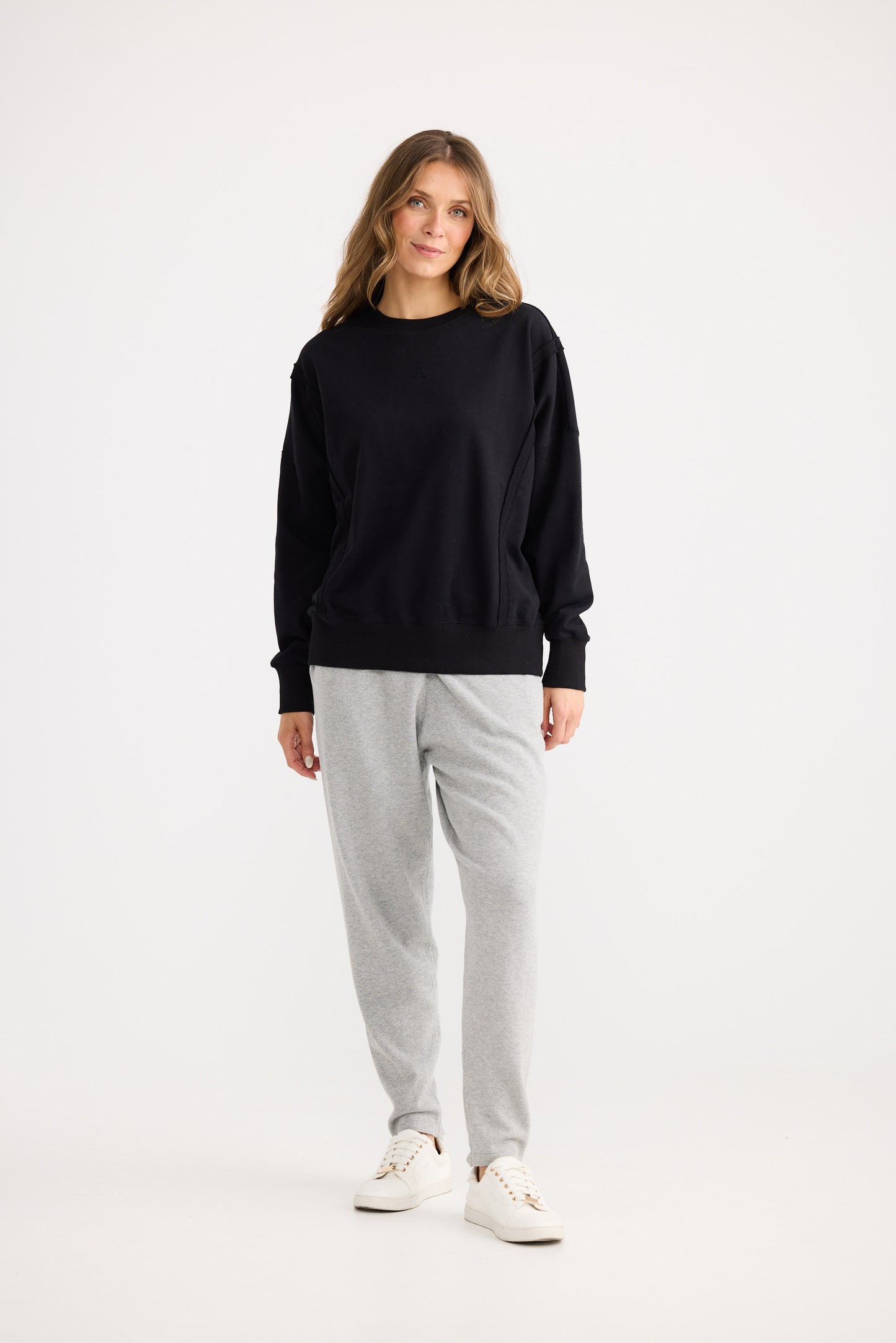 Woman wearing a black sweater and gray pants on a white background