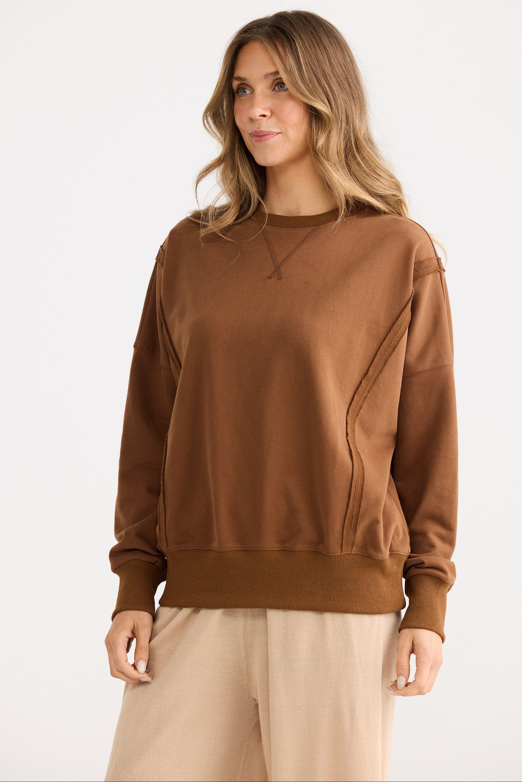 Woman wearing a brown sweatshirt and beige pants on a white background