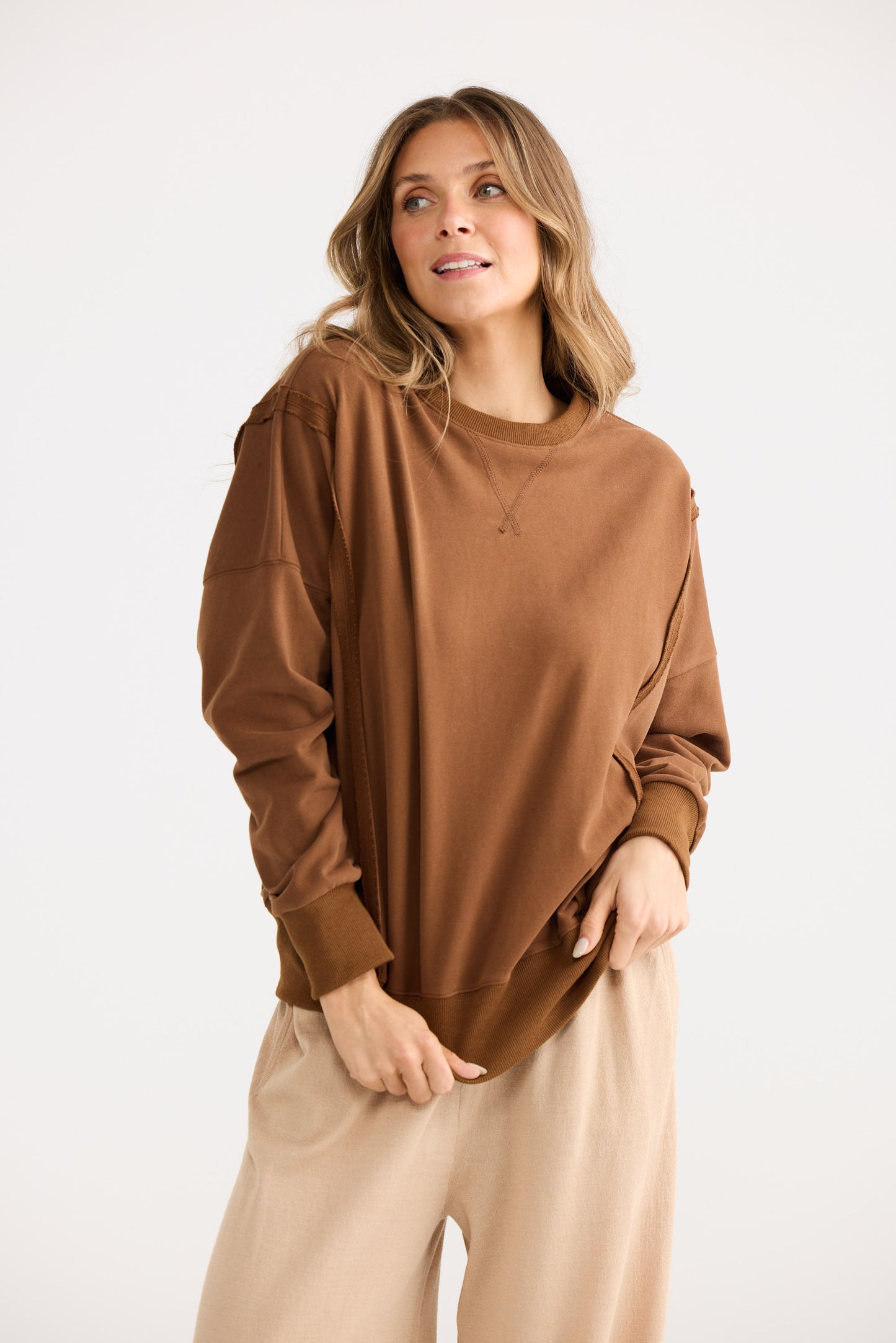 Woman wearing a brown sweater and beige pants on a white background