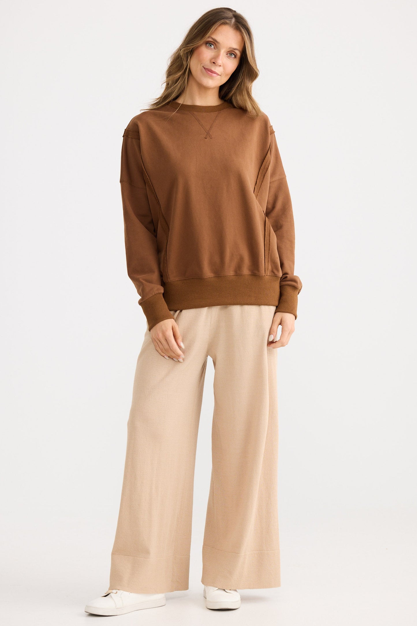 Woman wearing a brown sweater and beige pants on a white background