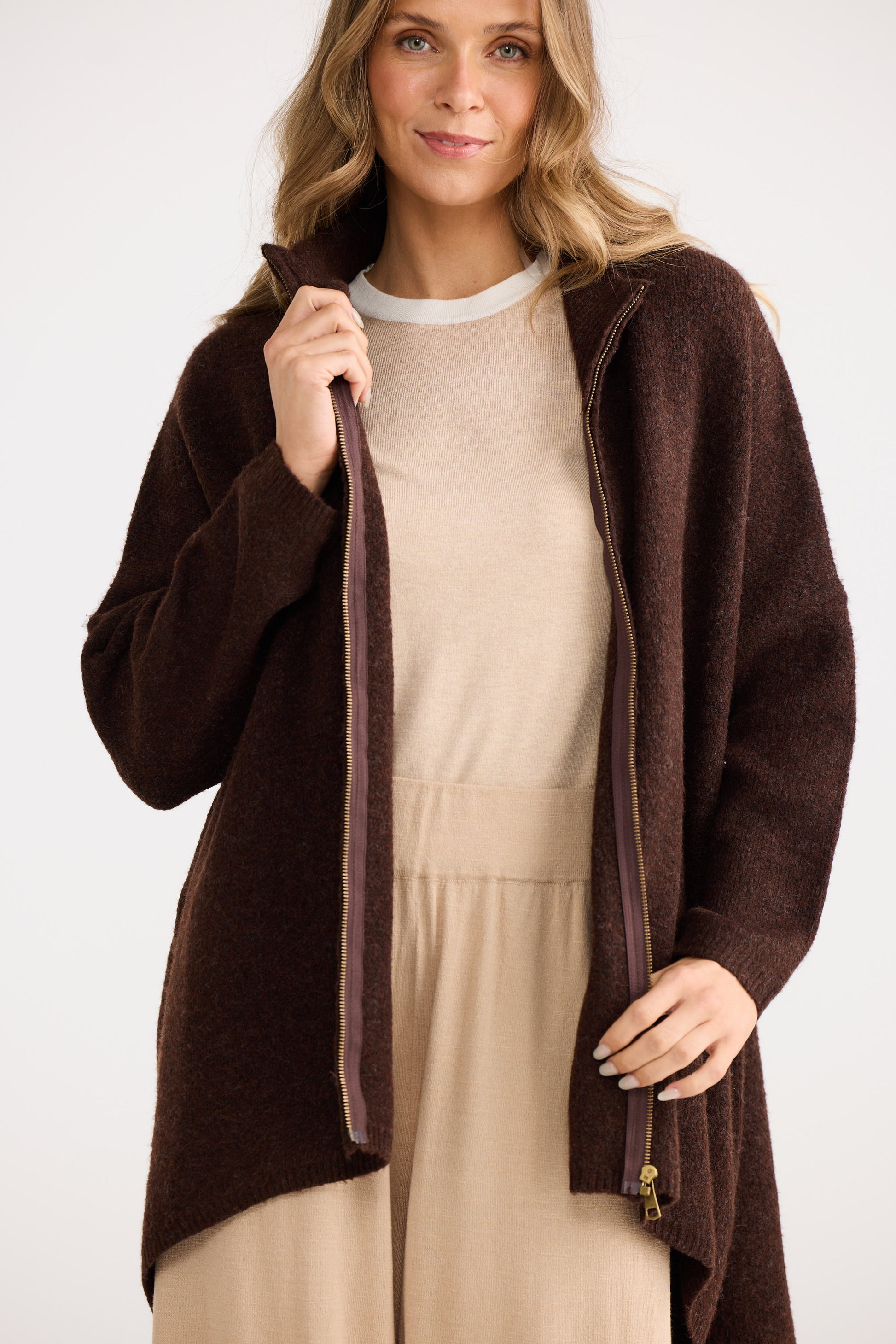 Woman wearing a brown cardigan over a beige dress on a white background