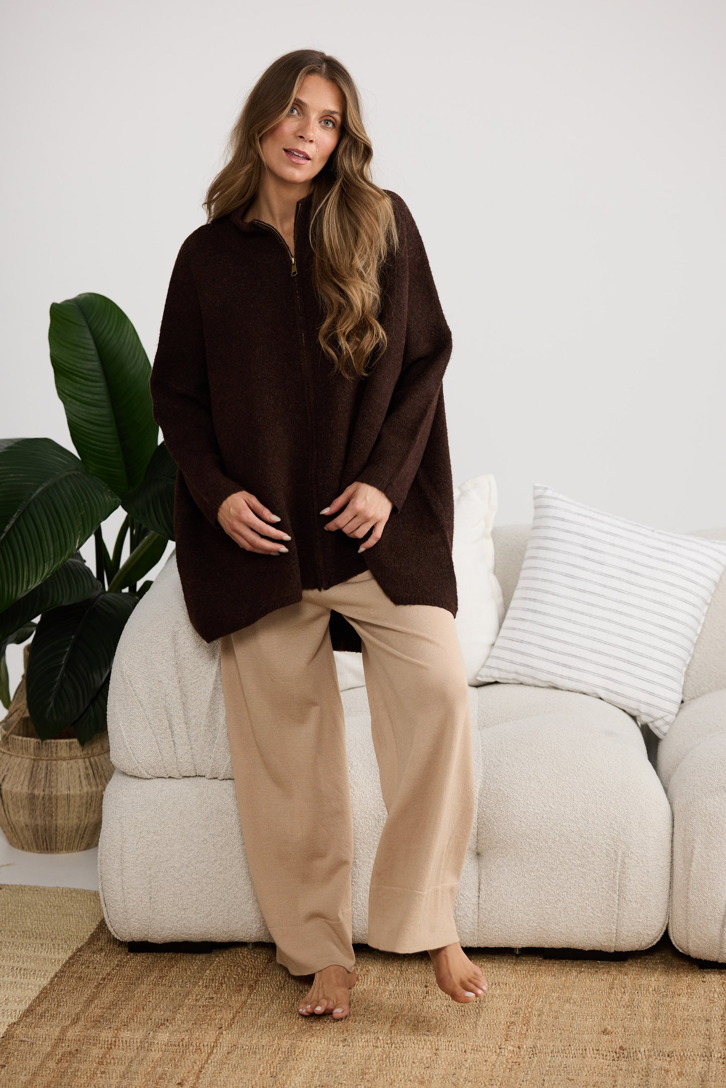 Woman wearing a brown poncho and beige pants standing in a living room.