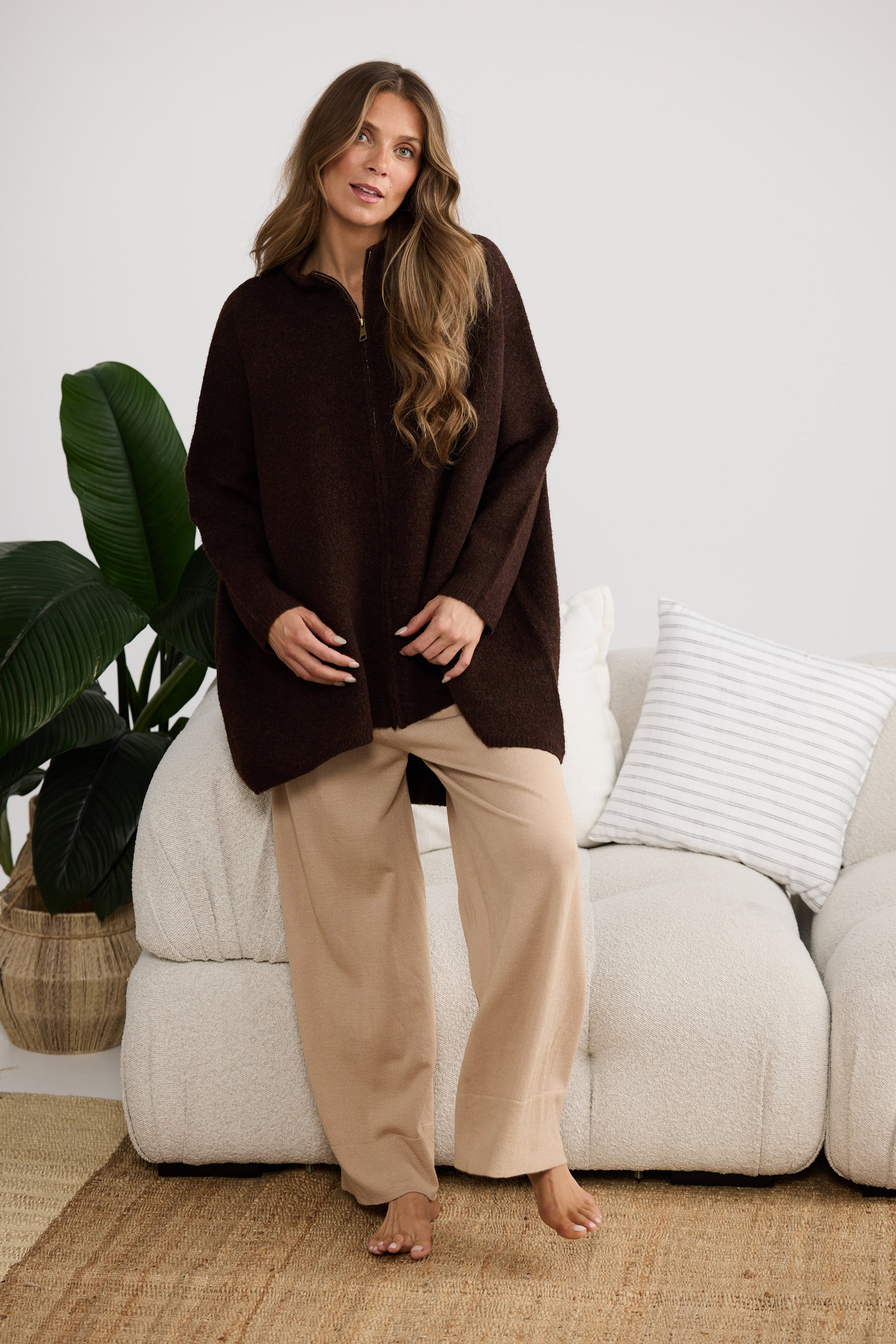 Woman wearing a brown poncho and beige pants standing in a living room.