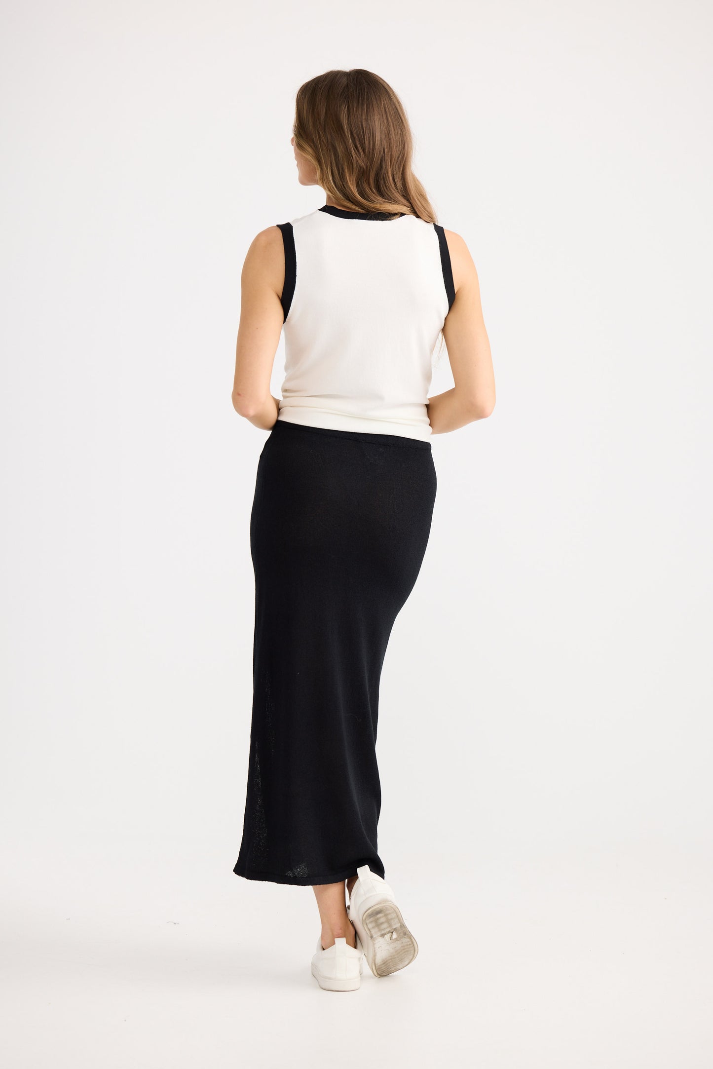 Woman wearing a white sleeveless top and black skirt on a white background