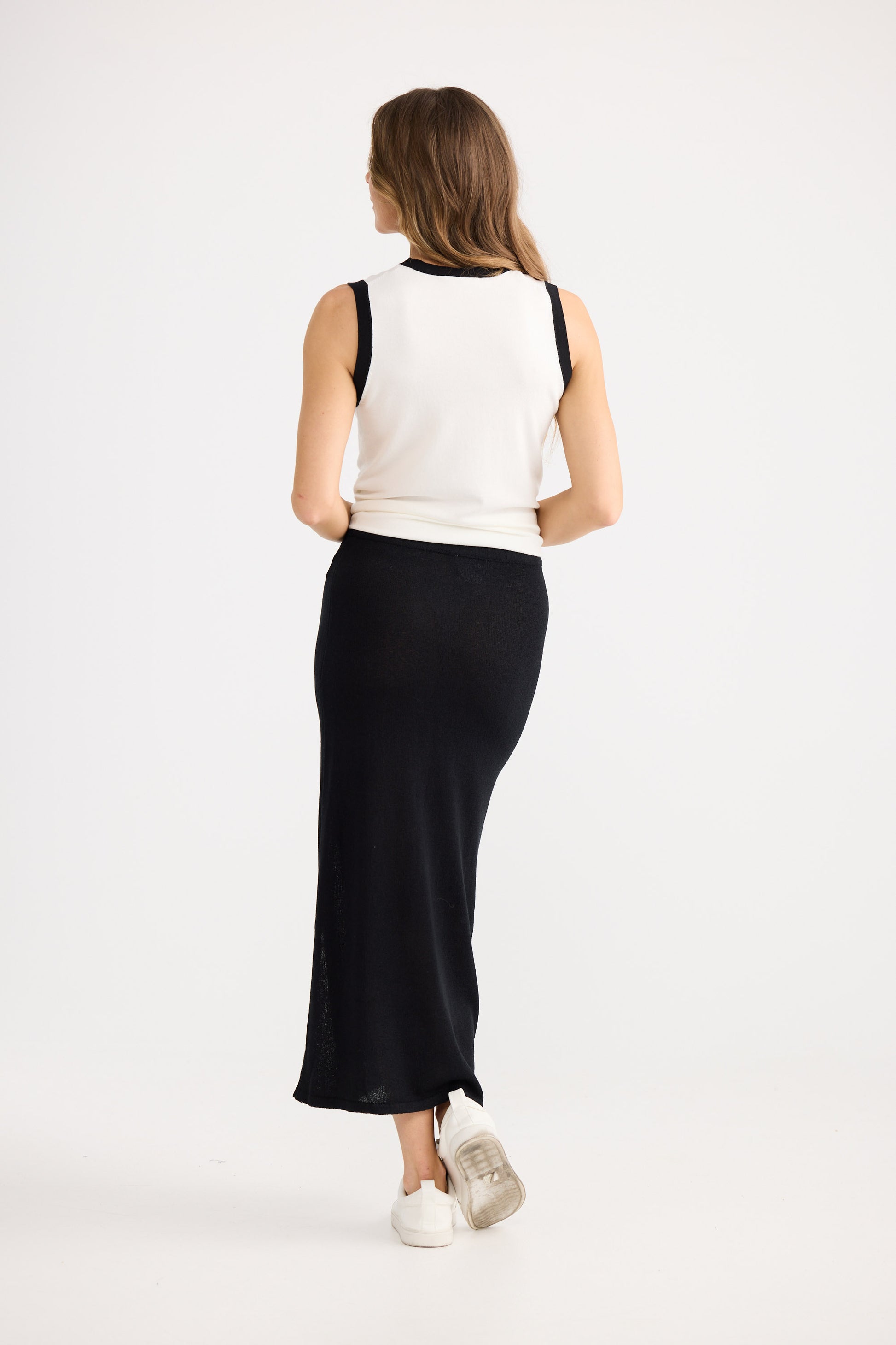 Woman wearing a white sleeveless top and black skirt on a white background