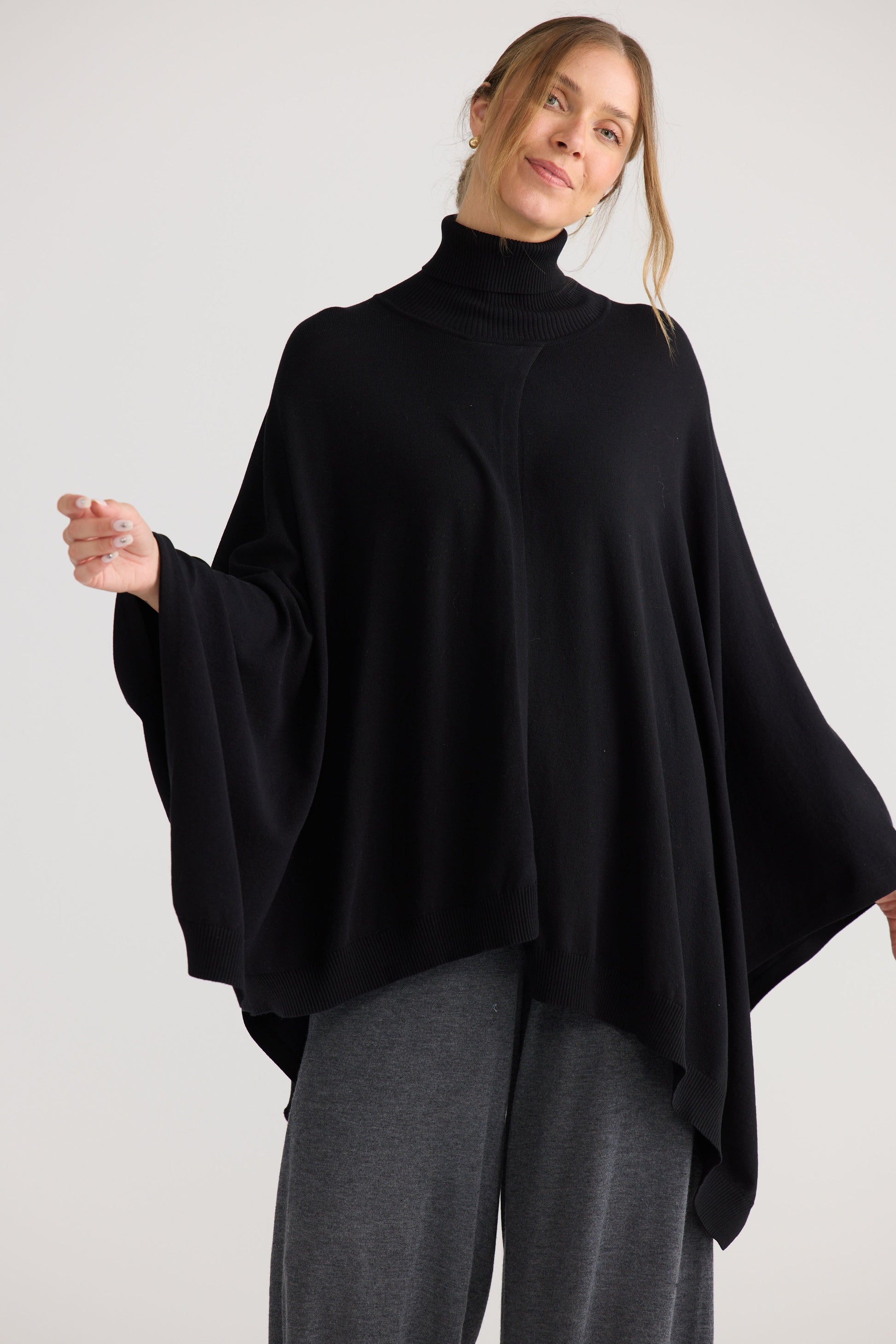 Model wearing Awaken Knit Cape in black, showing draped cape shape.