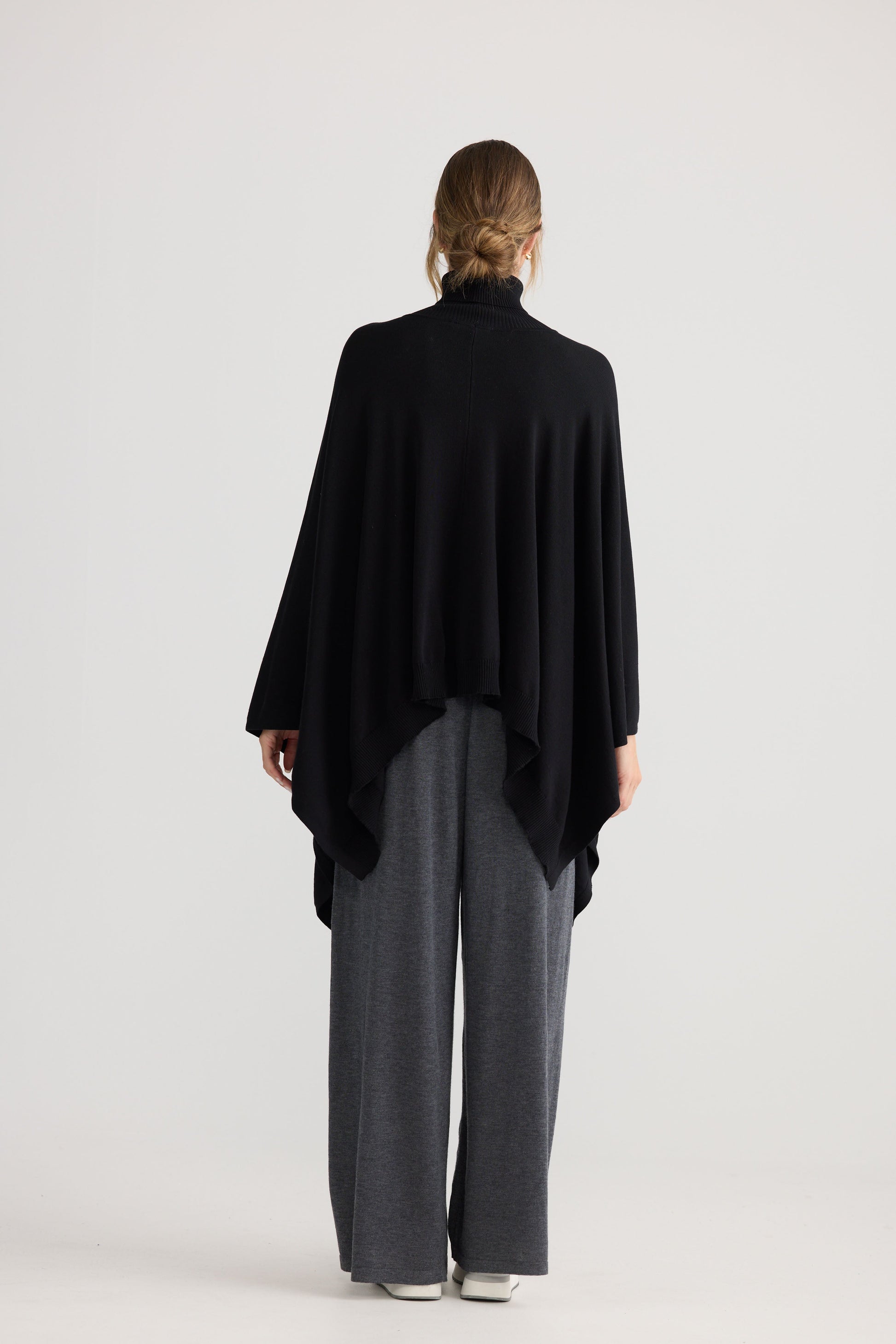 Awaken Knit Cape in black, styled with a relaxed outfit.