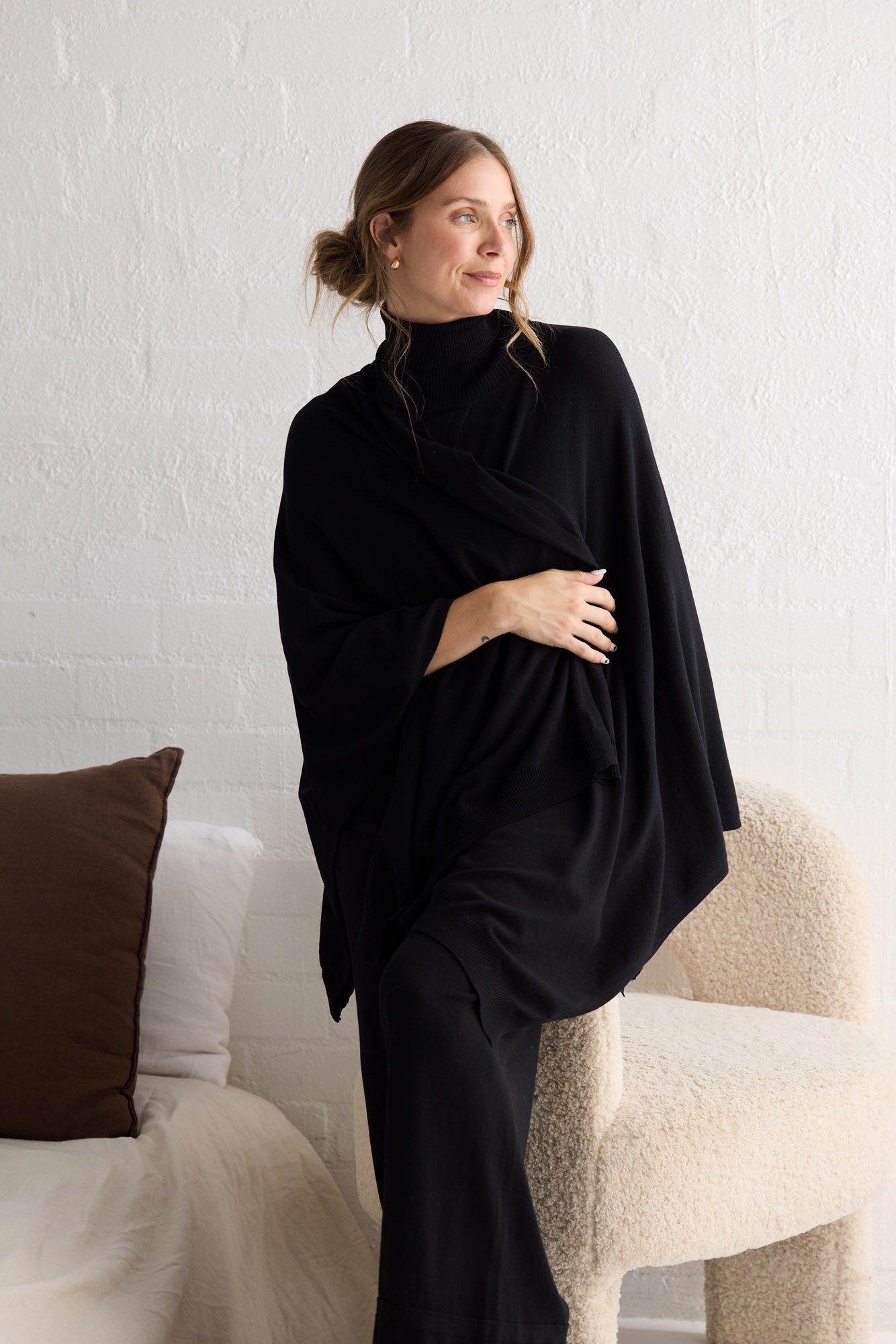 Campaign image of model wearing Awaken Knit Cape in black.