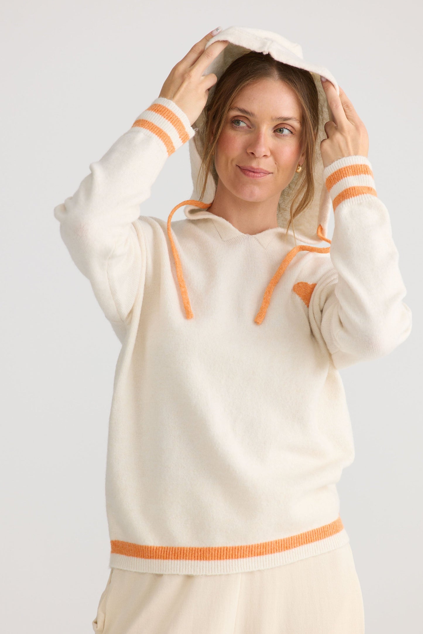 Model wearing Bold Hearts Hoodie in off white, showing hooded knit shape.